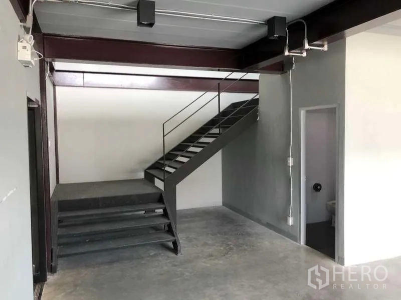 Warehouse for rent in Bang Phli, Samut Prakan - Ground floor area with metal staircase to mezzanine and adjacent restroom.