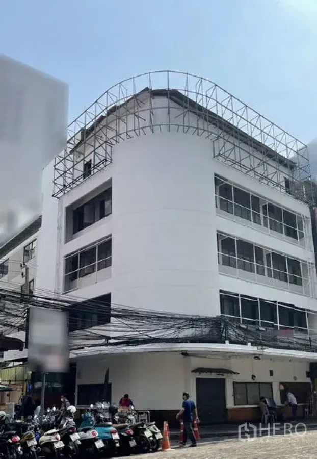Retail Space for rent in Bang Rak, Bangkok - White four-storey corner commercial building with wide windows and a rooftop steel frame, featuring a street-level storefront and motorbike parking in Silom.