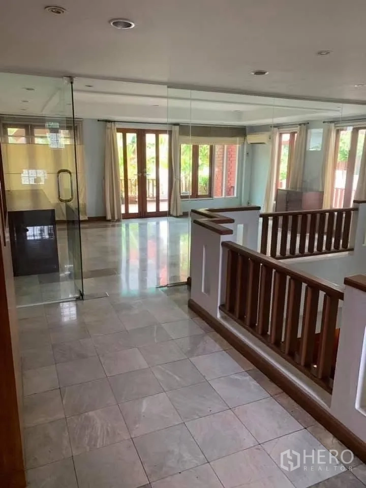 Townhouse for rent in Watthana, Bangkok - Upper landing with glass-walled room, marble tiles and wooden stair railings.