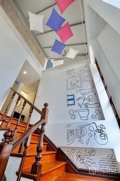 Shophouse for rent in Pathum Wan, Bangkok - Wood staircase with doodle wall art and a decorative ceiling net with cushions.