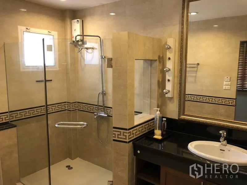 Detached House for rent or sale in Bang Kapi, Bangkok - Modern bathroom with glass-enclosed shower, vanity and beige tiles.