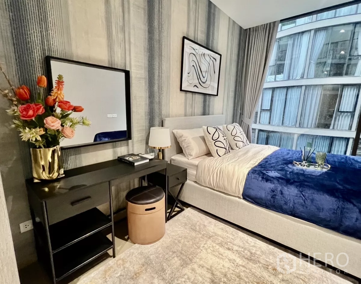 Condominium for rent in Khlong Toei, Bangkok - Bedroom with dressing desk, decorative flowers and an expansive window.