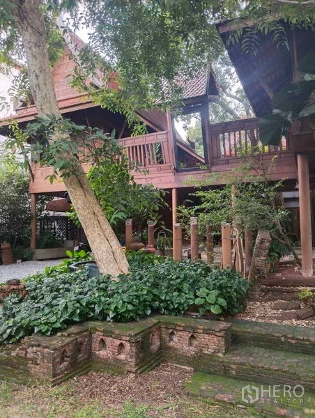 独立式住宅 出租或出售在Suan Luang, Bangkok - 连体泰式高脚屋，周围是成熟绿化与砖砌花坛。