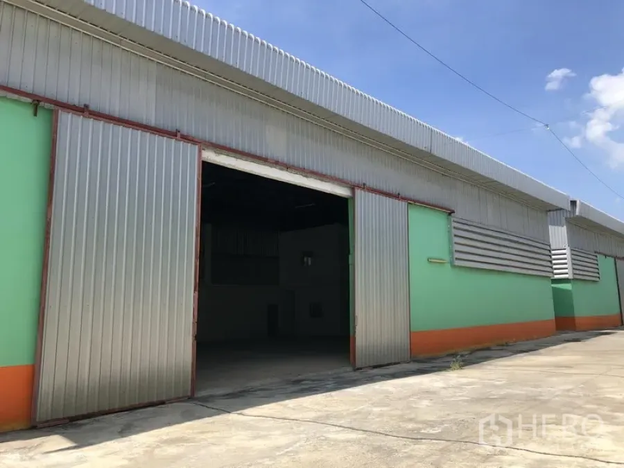 Warehouse for rent in Pathum Thani - Warehouse exterior with a large sliding metal door and ventilation louvers beneath a corrugated roof.