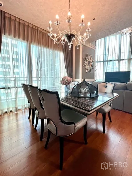 Condominium for rent in Khlong Toei, Bangkok - Dining table set beside tall windows with sheer curtains.