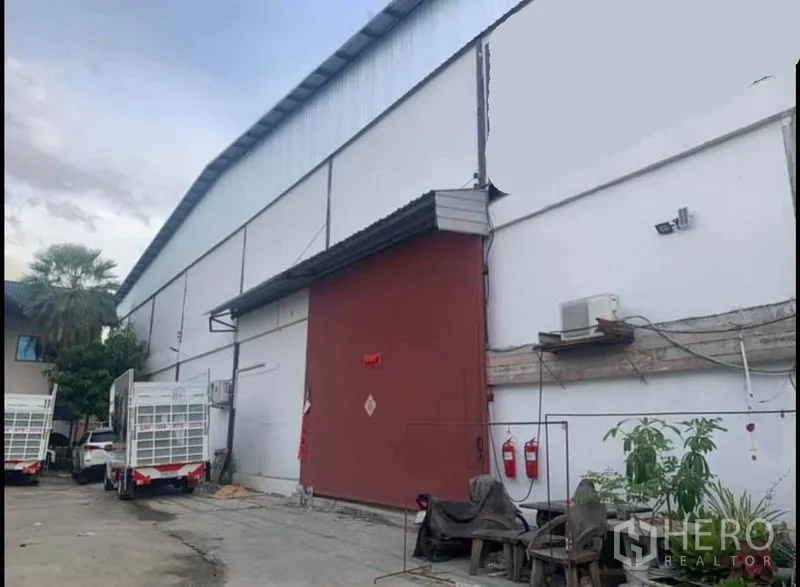 货栈 出租在Sai Noi, Nonthaburi - 大型白色仓库外观，红色滑门，高屋顶，装卸区与卡车