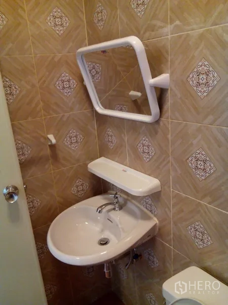 Shophouse for rent in Phra Khanong, Bangkok - Washbasin with shelf and framed mirror in a tiled bathroom.