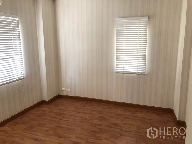 Detached House for rent or sale in Bang Kapi, Bangkok - Empty bedroom with wood flooring and two windows with blinds.