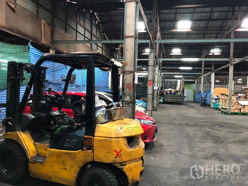 Warehouse for rent in Bang Kho Laem, Bangkok - Spacious warehouse interior with high metal roof, a forklift and parked vehicles for storage operations.
