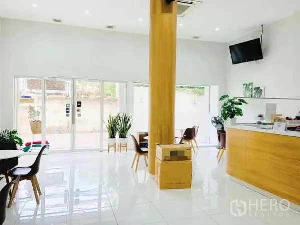 Shophouse for rent or sale in Khlong Toei, Bangkok - Open-plan front area with glass sliding storefront doors, wooden column, seating and a reception counter under recessed lighting.