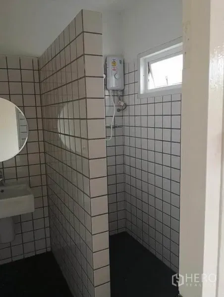 Townhouse for rent or sale in Din Daeng, Bangkok - Bathroom with white square tiles, separate shower area, small window, and a round mirror over the sink.