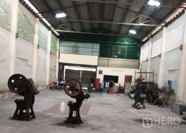 Warehouse for rent or sale in Pak Kret, Nonthaburi - Spacious warehouse interior with high steel-truss ceiling, ventilated glass-block walls and a large shutter door.