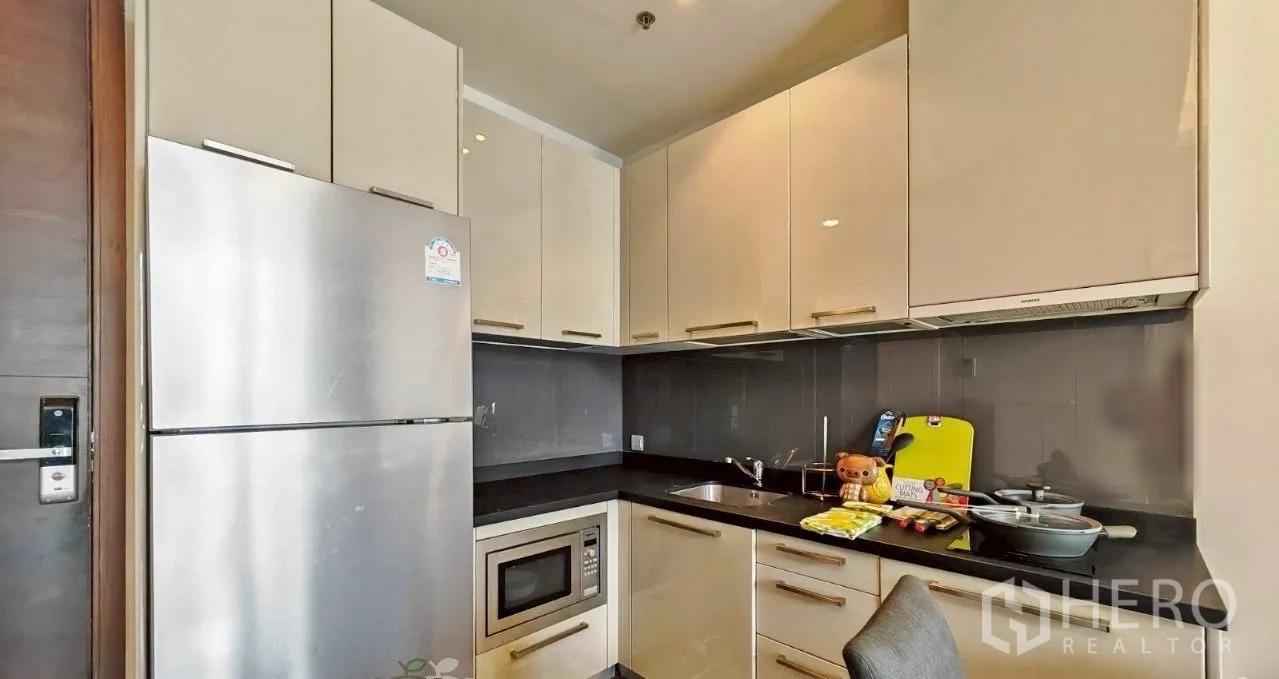 Condominium for rent in Watthana, Bangkok - Modern kitchenette with glossy cabinetry, black countertops, sink, microwave, and a large refrigerator.