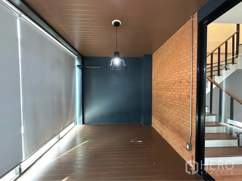 Townhouse for rent in Pak Kret, Nonthaburi - Industrial-style corridor with brick accent wall beside staircase and window blinds.