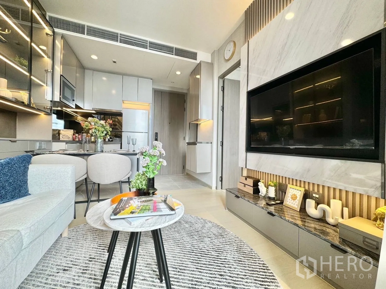 公寓 for rent in Ratchathewi, Bangkok - 开放式起居区，配有沙发、石纹电视墙以及带两人餐位的紧凑厨房。