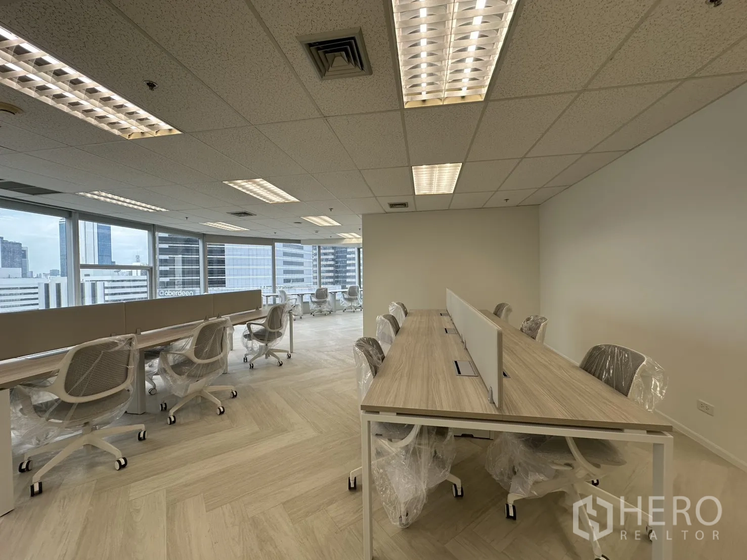 办公室 for rent in Sathon, Bangkok - 明亮的开放式办公室，长条工位与白色椅子，大窗俯瞰城市天际线。