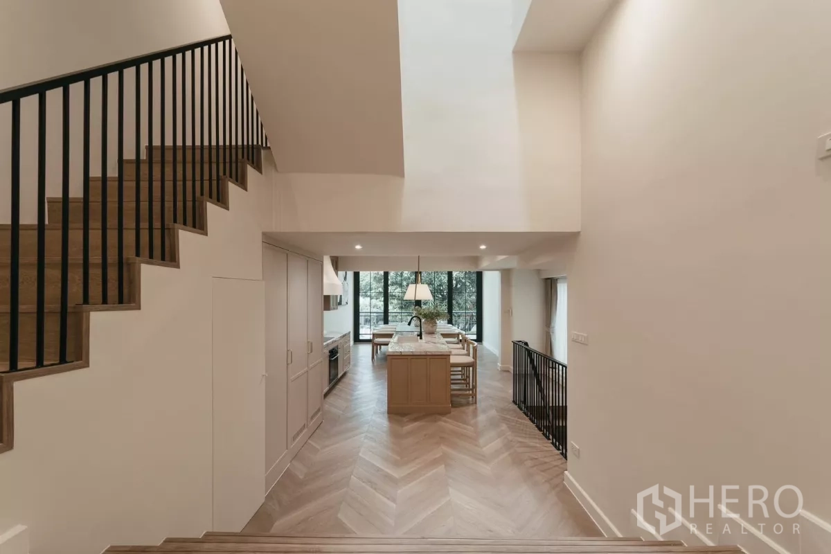 Townhouse for rent in Watthana, Bangkok - Split-level corridor leading to double-height kitchen and dining with glass doors.