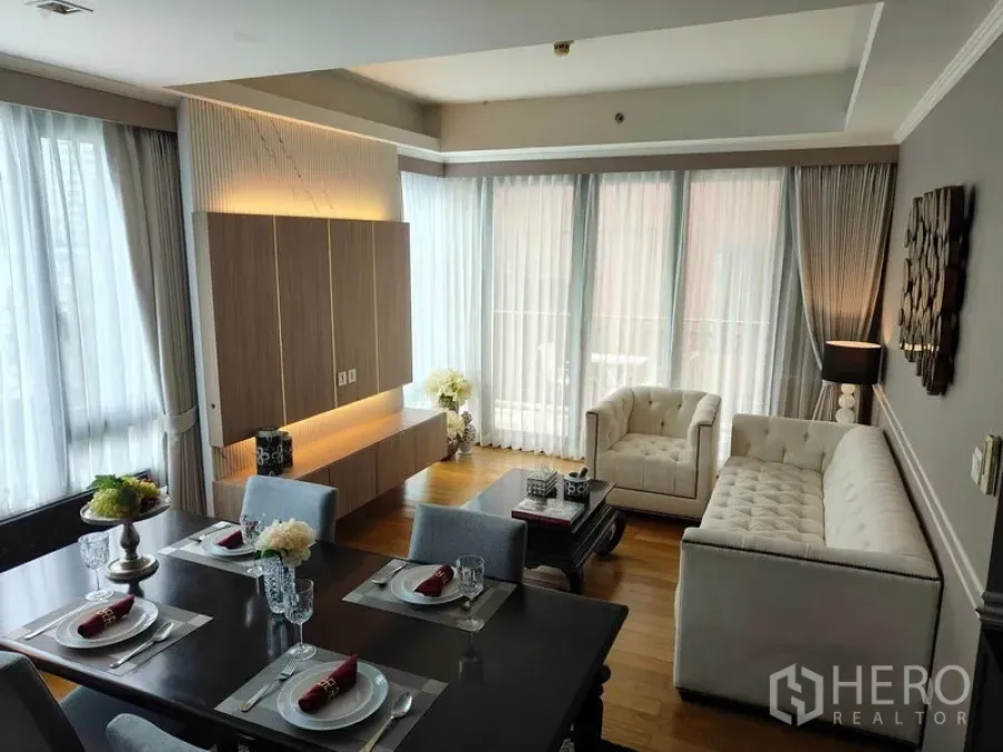Condominium for rent or sale in Pathum Wan, Bangkok - Open-plan living and dining room with bright windows, white sofas, and a set dining table leading to the balcony.