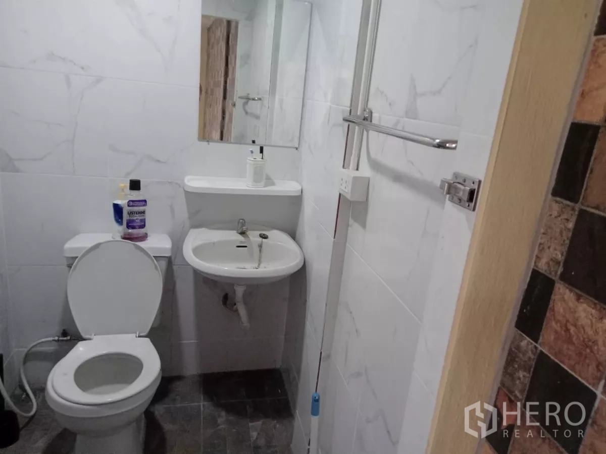 Detached House for rent in Phaya Thai, Bangkok - White-tiled ensuite bathroom with toilet, sink and mirror.