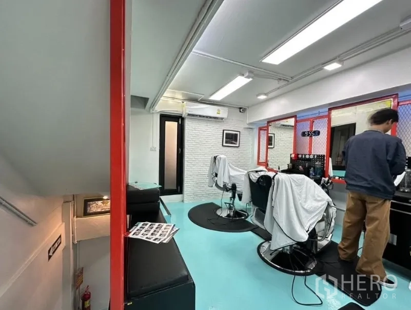 Shophouse for sale in Watthana, Bangkok - Bright salon-style interior with turquoise floor, mirrors, and barber chairs under linear ceiling lights.