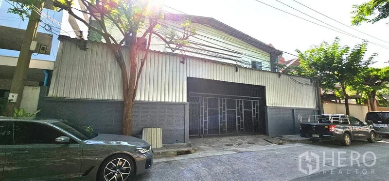 Warehouse for rent in Chatuchak, Bangkok - Street-facing metal-clad warehouse exterior in Chatuchak, Bangkok with wide gated entrance and shade trees.