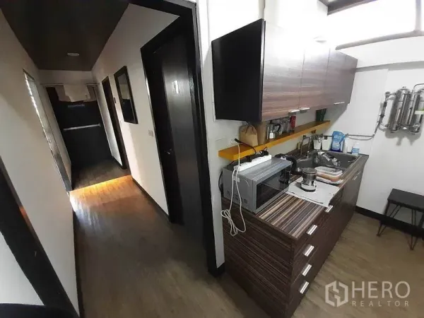 Office Space for rent in Khlong Toei, Bangkok - Compact pantry with sink, microwave and wood cabinetry along a corridor.