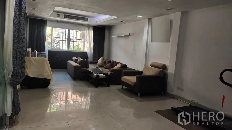 联排别墅 出租在Watthana, Bangkok - 明亮客厅，沙发组、大窗与吊顶射灯。
