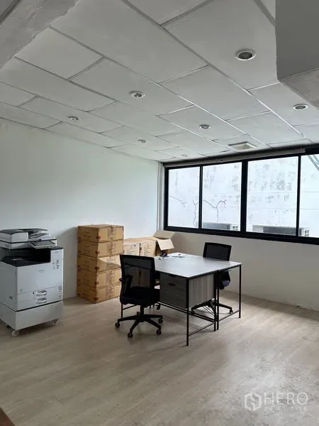 店屋 出租在Khlong Toei, Bangkok - 明亮办公室，两个工位、打印机与靠窗堆放的纸箱。