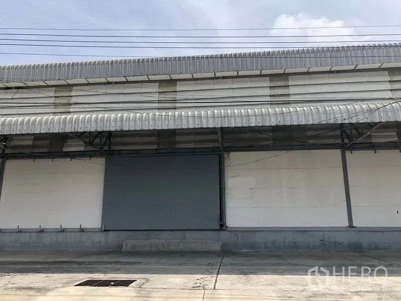 Warehouse for rent in Khlong Luang, Pathum Thani - Warehouse exterior with covered loading bay, roller shutter door and wide concrete apron.