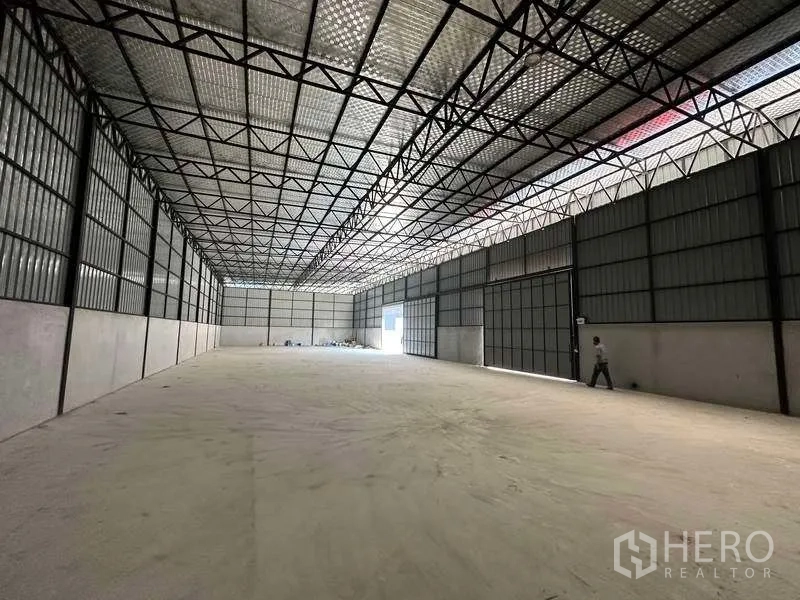 Warehouse for rent in Khlong Sam Wa, Bangkok - Long storage hall with lattice roof, skylight strips and oversized access doors along one wall.