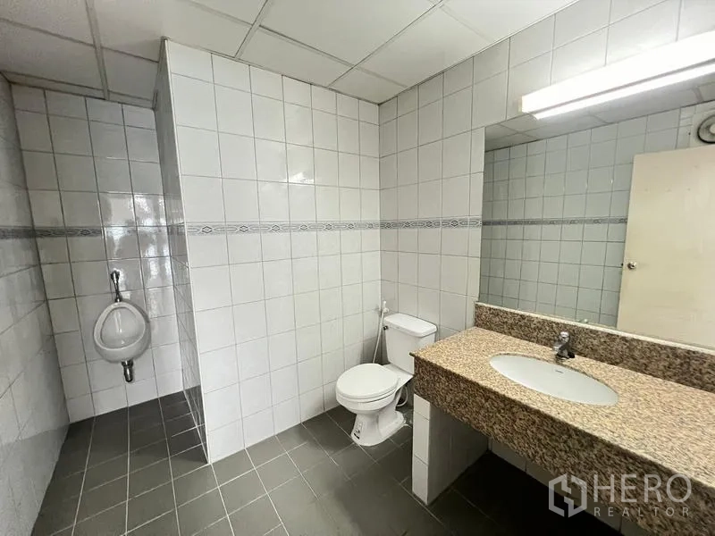Office Space for rent or sale - Tiled office bathroom with granite vanity, large mirror, toilet, and urinal.