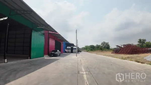 Warehouse for rent in Mueang Chachoengsao, Chachoengsao - Row of warehouses along a wide concrete road with truck access and open land on the side.