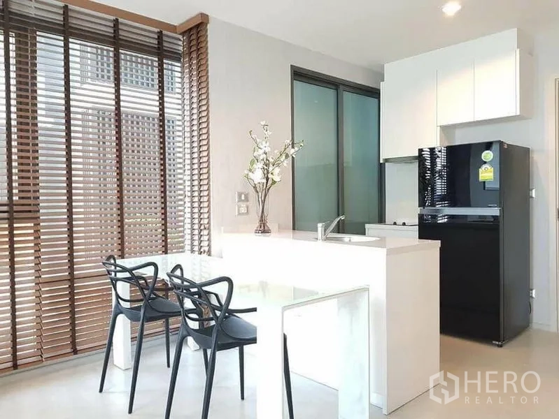 Condominium for rent or sale in Khlong Toei, Bangkok - Modern kitchen island with sink and three dining chairs next to tall wooden blinds.
