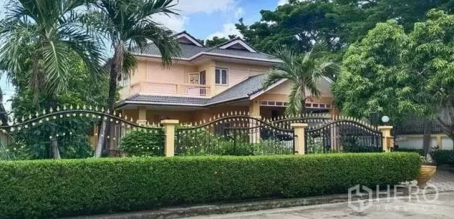 Detached House for sale in Prawet, Bangkok - Street view of house with wrought-iron fence, palm trees and lush greenery.