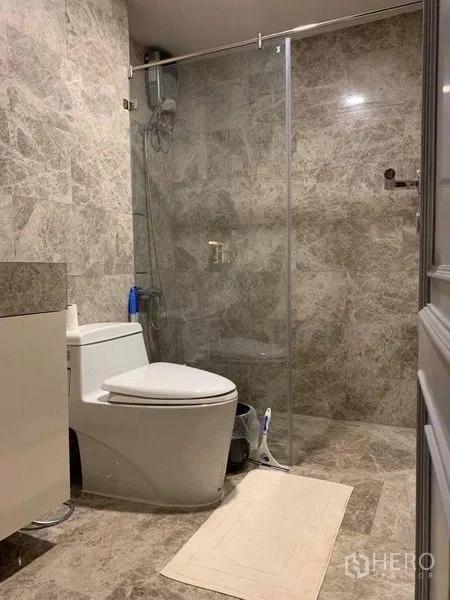 Condominium for sale in Khlong Toei, Bangkok - Bathroom clad in marble tiles with glass-enclosed shower and contemporary sanitary ware.