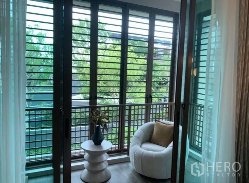 Detached House for sale in Bang Kapi, Bangkok - Upper-floor balcony with louvered screens, accent chair and views of trees for natural ventilation.