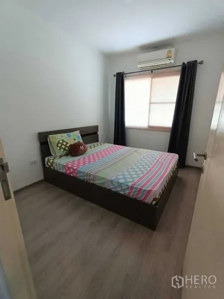 Townhouse for rent in Prawet, Bangkok - Compact bedroom with bed, window blinds, dark curtains and wall-mounted air conditioner.