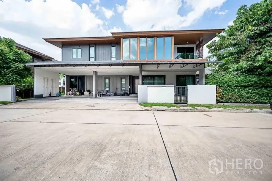 Detached House for sale in Prawet, Bangkok - Front exterior with wide carport, tall windows and gated entrance on a quiet street.