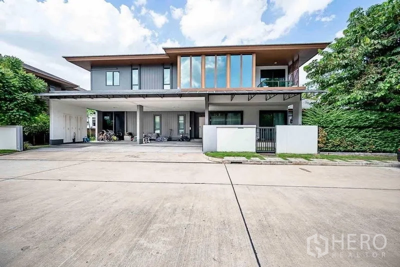Detached House for sale in Prawet, Bangkok - Front exterior with wide carport, tall windows and gated entrance on a quiet street.