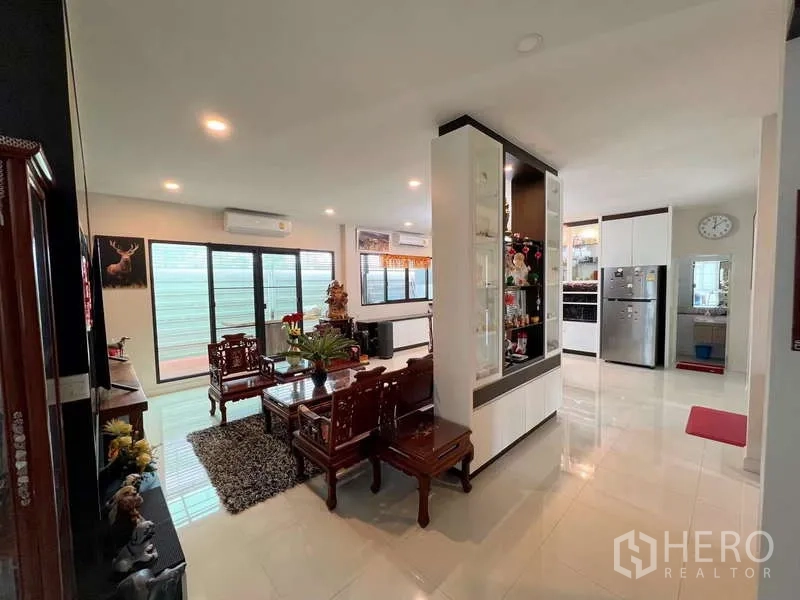 Detached House for sale in Prawet, Bangkok - Open-plan living and dining area with carved wooden furniture, glass display cabinets, and sliding doors.