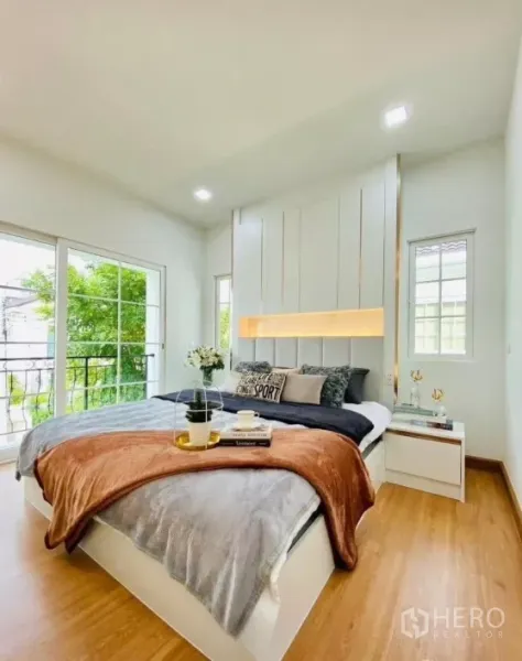 Detached House for rent in Prawet, Bangkok - Bright master bedroom with large windows, sliding doors to a balcony and wood flooring overlooking greenery.