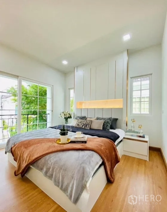 Detached House for rent in Prawet, Bangkok - Bright master bedroom with large windows, sliding doors to a balcony and wood flooring overlooking greenery.