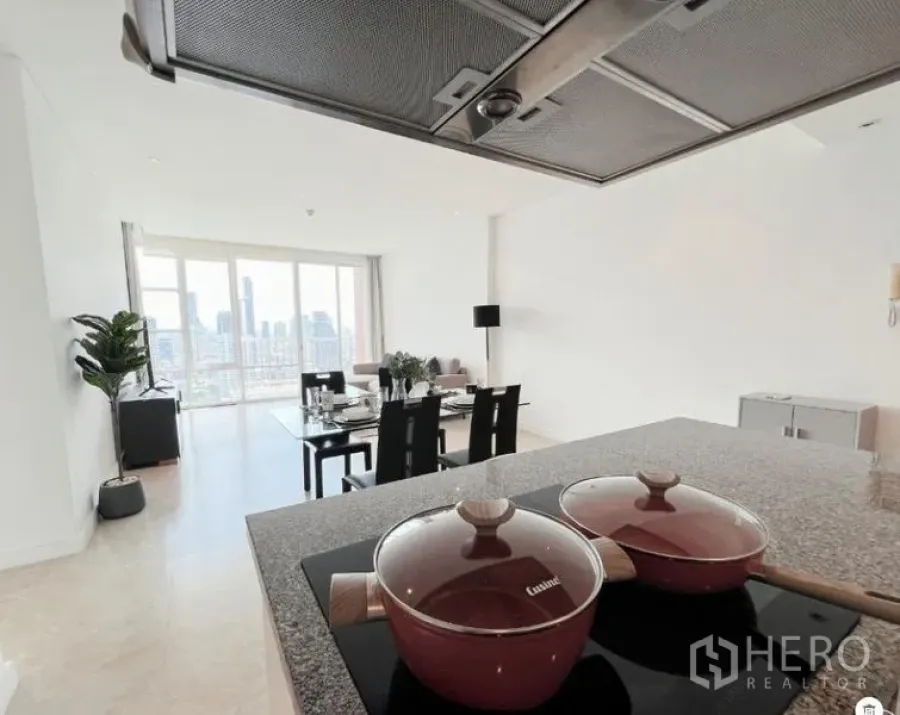 Condominium for sale in Watthana, Bangkok - Cooktop and range hood overlooking the dining table and tall windows with city view.