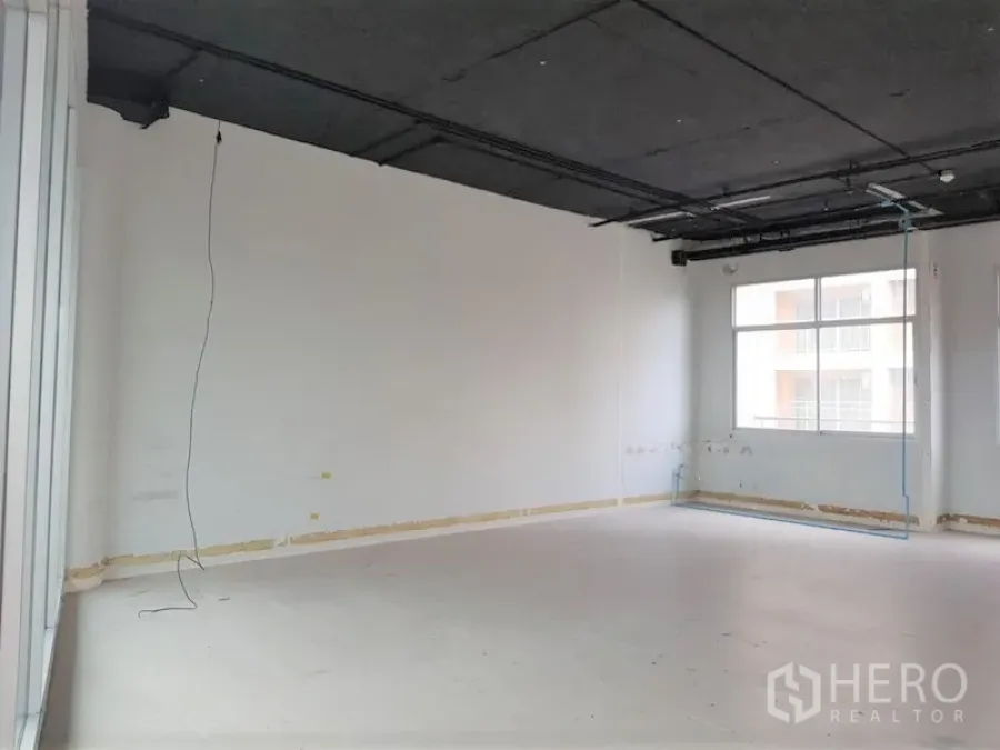 Office Space for rent in Phra Khanong, Bangkok - Unfurnished open-plan office with exposed black ceiling, white walls, and a large window allowing natural light.