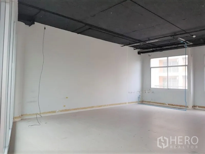 Office Space for rent in Phra Khanong, Bangkok - Unfurnished open-plan office with exposed black ceiling, white walls, and a large window allowing natural light.