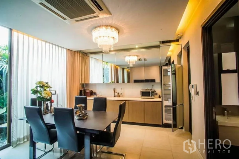 Townhouse for rent or sale in Watthana, Bangkok - Dining space and modern kitchen with mirrored backsplash and built-in appliances