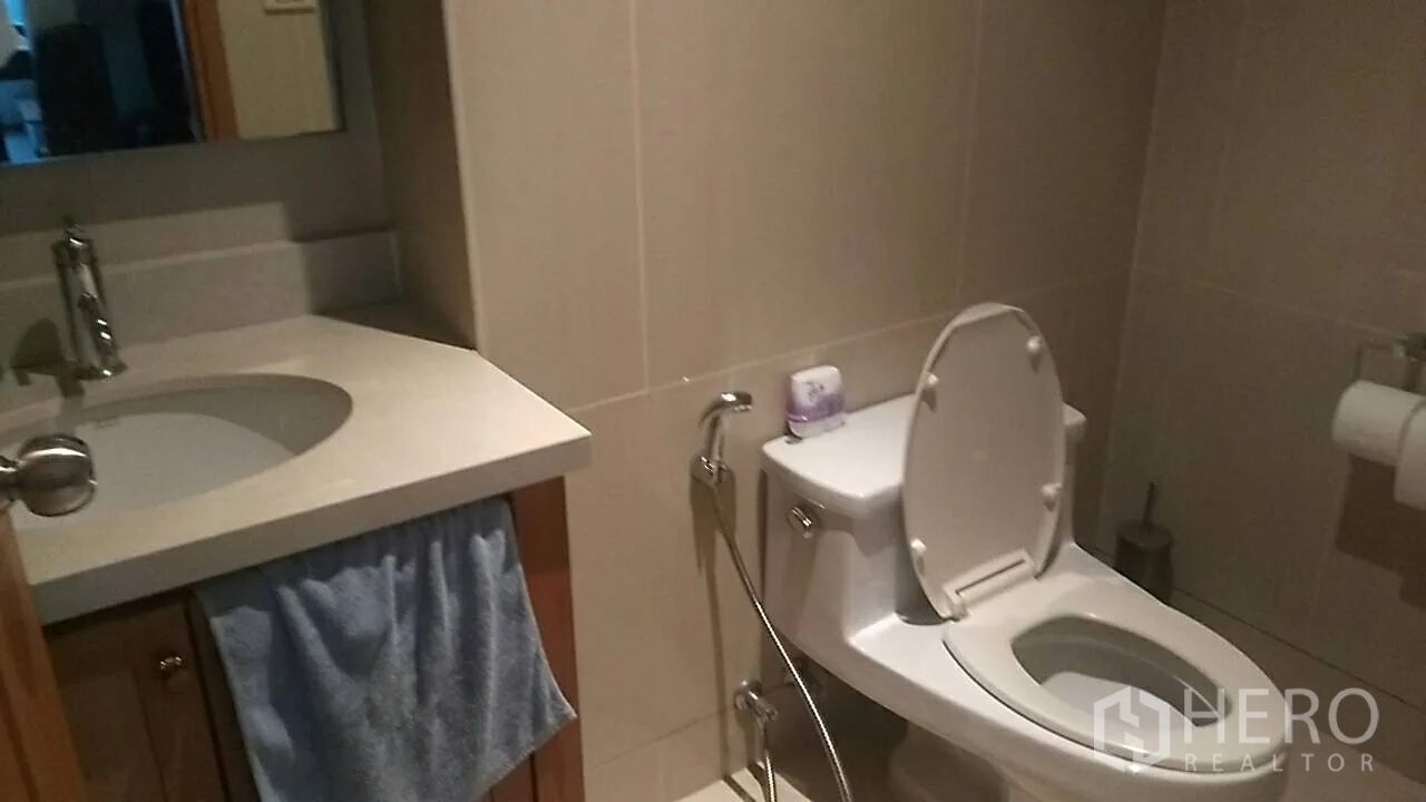 Condominium for sale in Khlong Toei, Bangkok - Tiled bathroom with vanity sink and toilet with bidet spray.