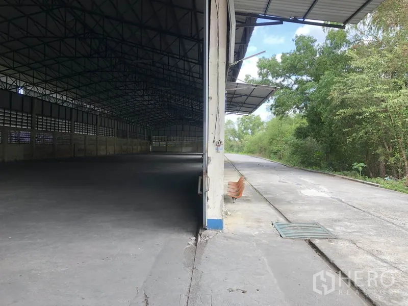 Warehouse for rent in Pathum Thani - Covered loading edge of the warehouse beside a service road and green trees.