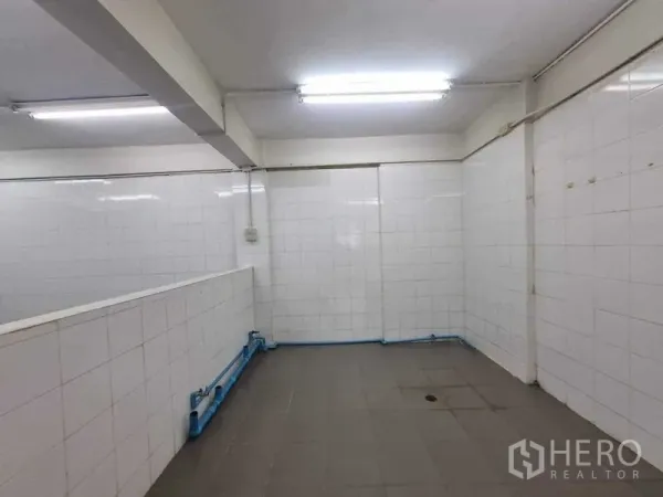Retail Space for rent in Bang Rak, Bangkok - Tiled back-of-house room with fluorescent lighting and visible blue plumbing, suitable for prep or wash area.