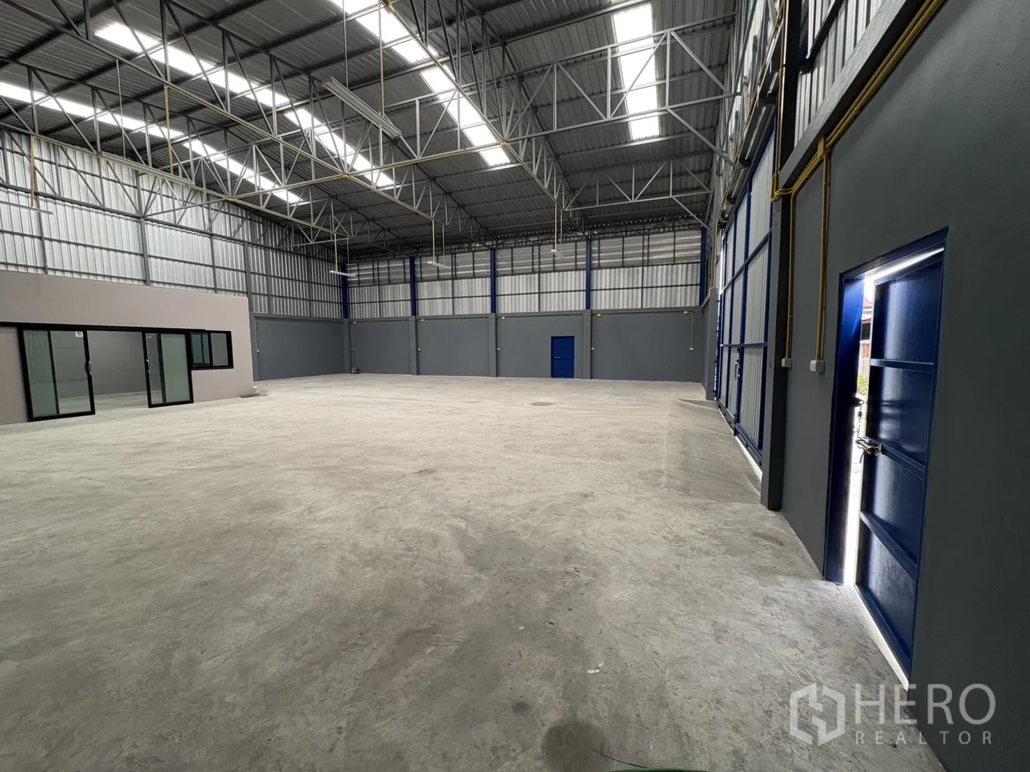 Warehouse for rent in Bang Phli, Samut Prakan - Open storage area featuring the glass office entrance, side service door, and high-bay lighting.